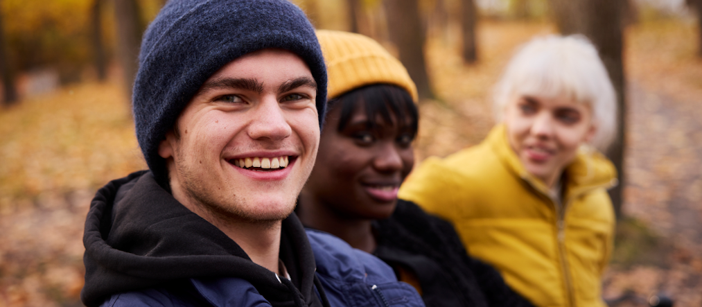 tre ungdomar sitter på en bänk i en bokskog om hösten.