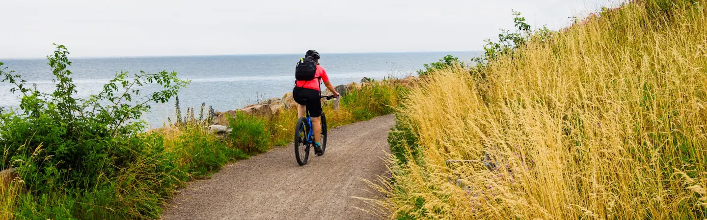 Person cyklar på grusad väg på en kulle längs med kusten.